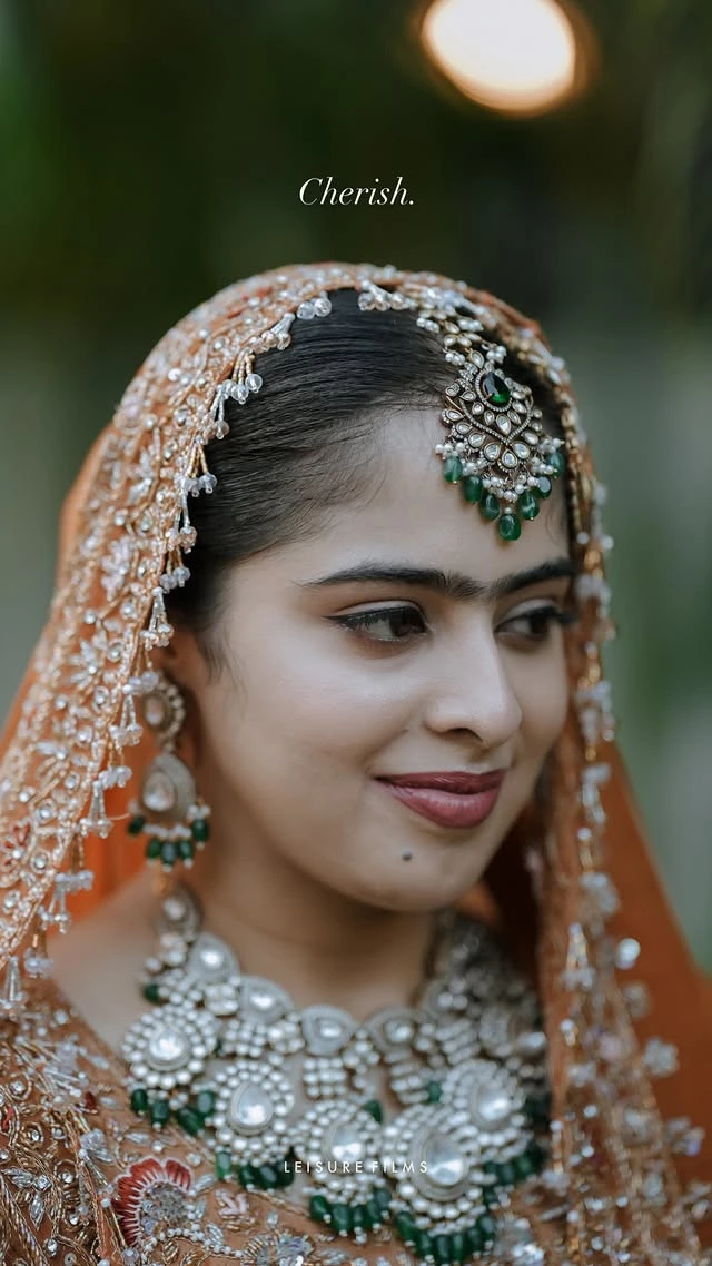 prettiest bride in orange lehanga facing down giving a little smile on her face perfectly captured by bes wedding photographer in calicut