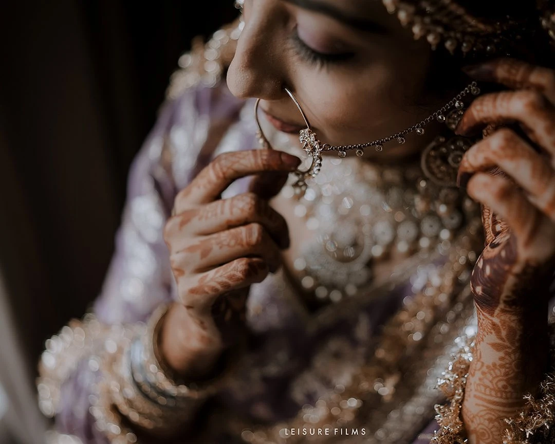 A bride delicately adjusting her nose ring, with intricate mehndi designs on her hands and ornate jewellery sparkling, beautifully captured by the best wedding photographer in Calicut.