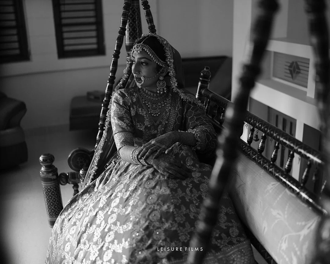 Elegant bride in traditional attire with intricate jewelry and mehndi, sitting gracefully on a wooden swing, beautifully photographed in black and white by the best wedding photographer in Calicut
