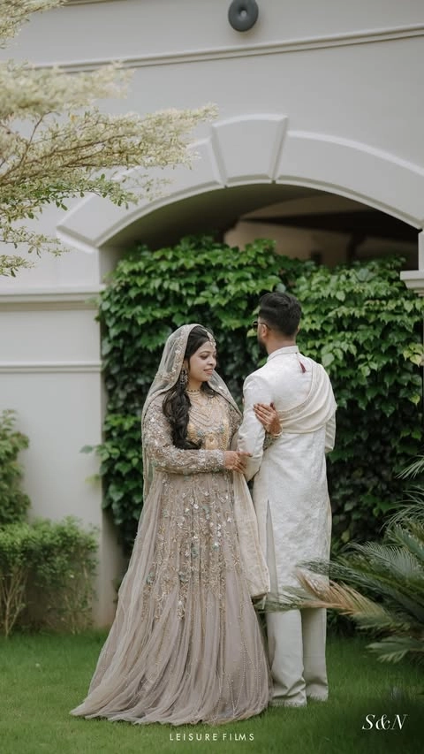 A bride in an embellished gown smiles at the groom dressed in a white sherwani as they share a tender moment in a lush garden, beautifully captured by the best wedding photographer in Calicut.